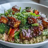 A close-up of the Quinoa Vegetable Teriyaki Bowl garnished with sesame seeds and fresh green onions, served steaming hot on a table.