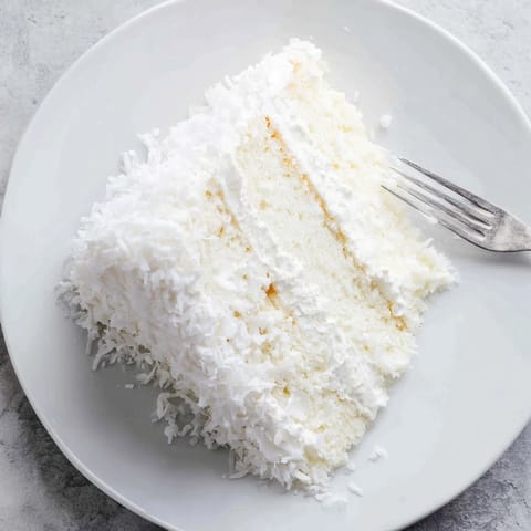 A freshly sliced wedge of Classic Coconut Cake reveals moist white layers and luscious coconut filling, served on a dessert plate.