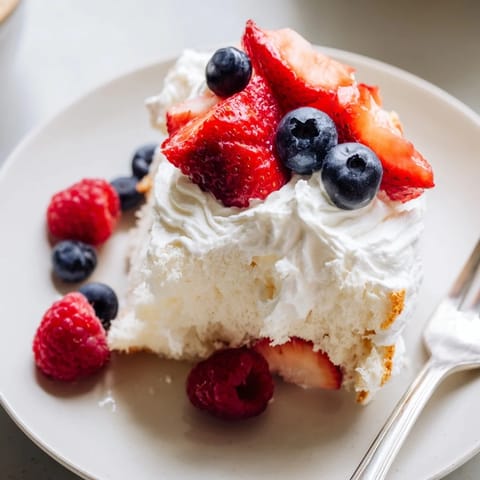 Freshly sliced Angel Food Cake on a plate, topped with a dollop of whipped cream and vibrant summer berries.