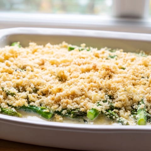 Steamed asparagus spears nestled in a rich, creamy Gruyère sauce inside a baking dish.