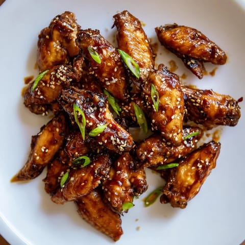 Golden-brown Asian Sticky Wings fresh from the oven, glistening with a thick, caramelized soy-ginger glaze and sprinkled with sesame seeds and green onions. 