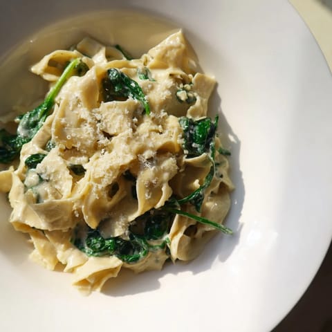 Steaming bowl of Creamy Spinach Garlic Noodles featuring golden egg noodles tossed with garlic and bright baby spinach.  