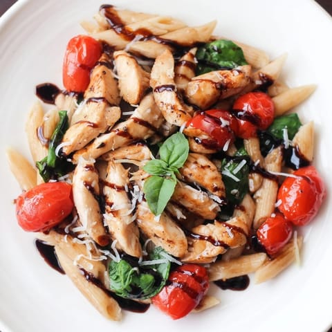 Creamy balsamic glazed chicken pasta served on a white plate, garnished with fresh basil and shaved Parmesan.