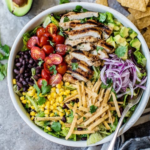 A vibrant plate of Honey Lime Chicken Taco Salad with grilled chicken, romaine, black beans, corn, avocado, and tortilla strips.
