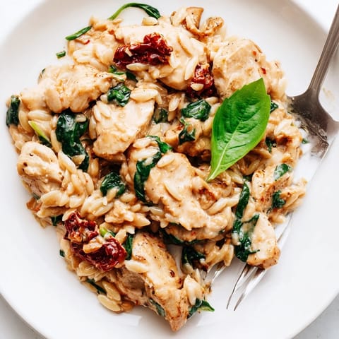 Tuscan Chicken Orzo is served steaming in a skillet, garnished with fresh basil and extra grated Parmesan.