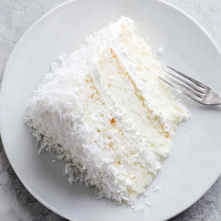 A freshly sliced wedge of Classic Coconut Cake reveals moist white layers and luscious coconut filling, served on a dessert plate.
