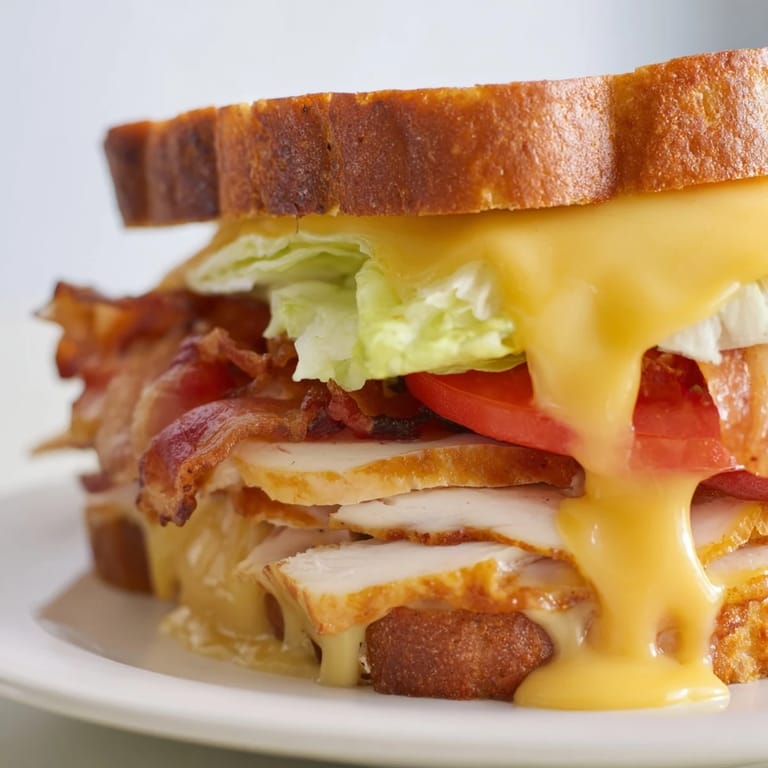 A close-up of a hot Turkey Club Grilled Cheese, featuring layers of roasted turkey, crunchy bacon, and melted cheese on crispy sourdough bread.