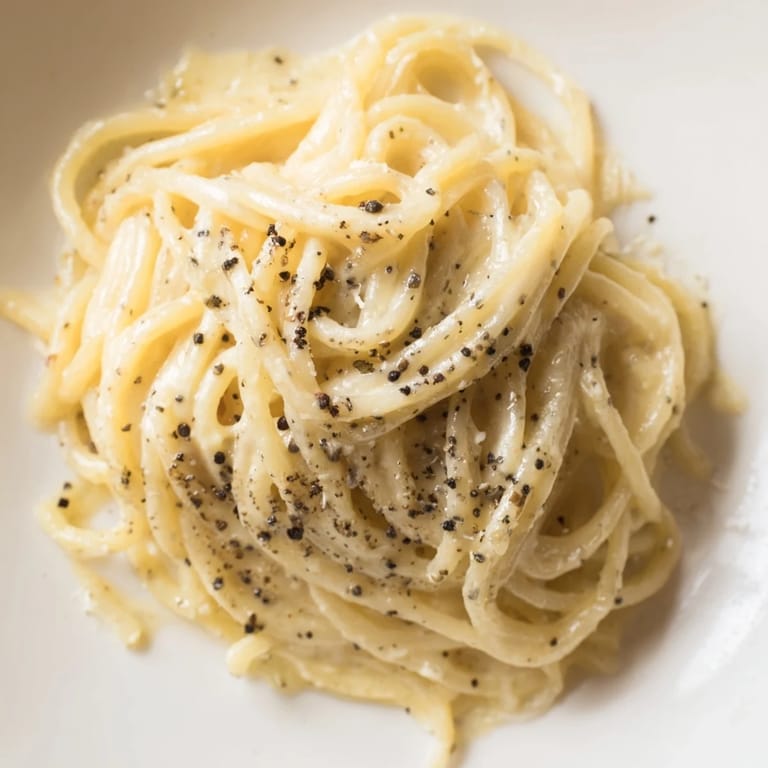 Ready-to-serve Spaghetti Cacio e Pepe in a white bowl, garnished with extra Pecorino and a glass of Pinot Grigio.