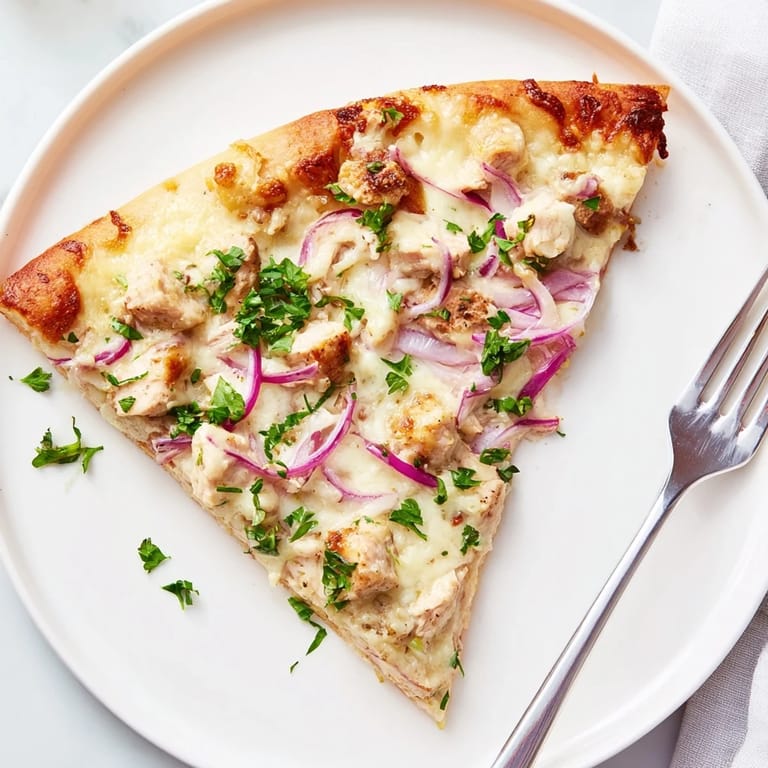 A slice of Chicken Alfredo Pizza lifted to reveal creamy Alfredo sauce, tender chicken, and bubbly cheese on a golden, flaky Italian-American crust.  