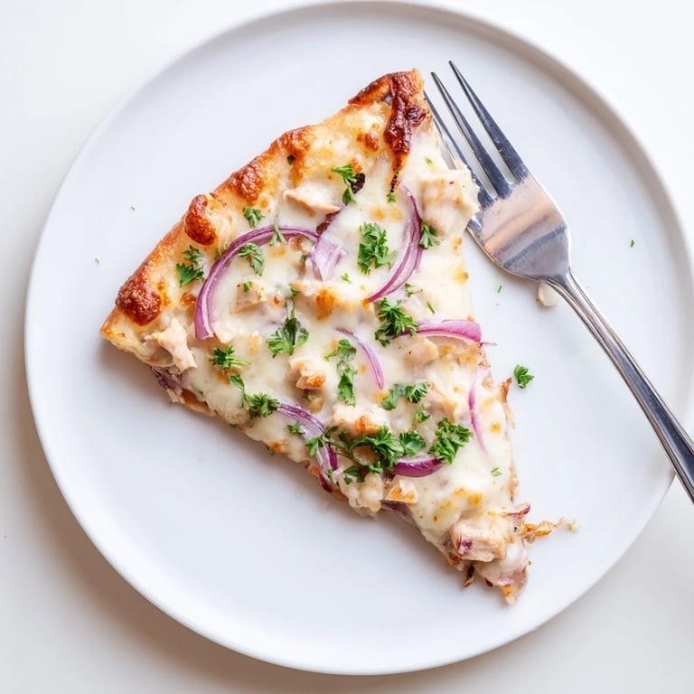 Freshly baked Chicken Alfredo Pizza garnished with parsley and red onion, paired with a glass of white wine on a rustic wooden table.