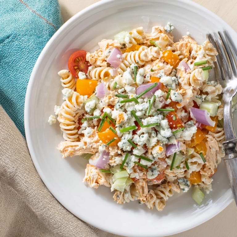 Zesty cold Buffalo Chicken Pasta Salad garnished with blue cheese and chives, ready for a picnic potluck.