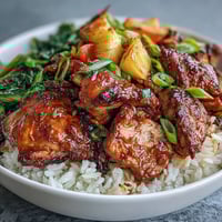 Cubes of tender chicken in glossy teriyaki glaze sit over fluffy white rice, with broccoli, carrots, and bright red peppers.